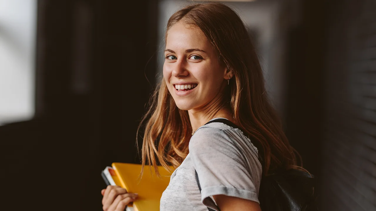 young student standing in hallway with books in hand